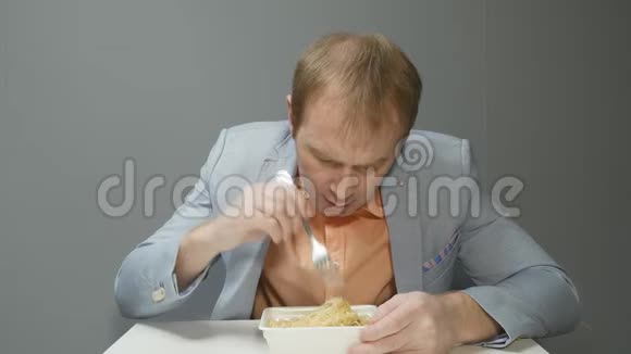 一个穿着蓝色夹克和橙色衬衫的年轻人正在吃方便面他仔细地把盘子里的东西混在一起视频的预览图