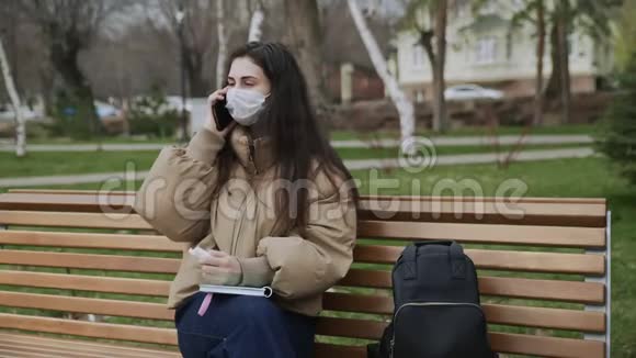 戴防护面具的年轻女子在城市公园写日记大流行Covid19冠状病毒保护视频的预览图