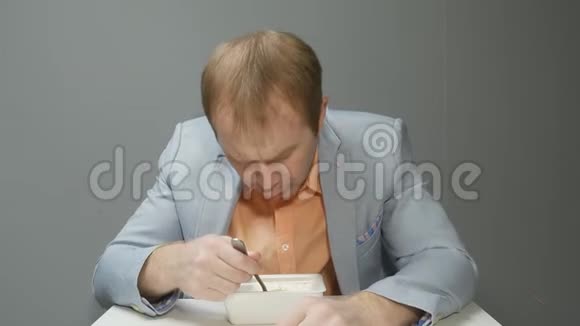 一个年轻的帅哥用叉子吃方便面他穿一件蓝色夹克和一件粉红色衬衫他看着视频的预览图