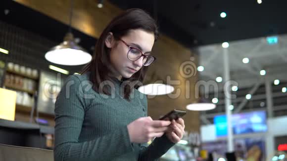 一个年轻的女人坐在一家带着电话的咖啡馆里女孩在智能手机上通信喝咖啡关闭视频的预览图