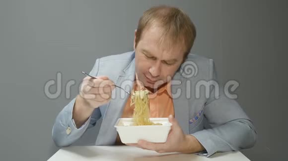 一个穿着蓝色夹克和粉红色衬衫的年轻人正在用叉子吃面条他高高举起叉子咀嚼视频的预览图