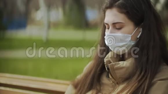 年轻女子戴着防护面具在城市公园使用智能手机进行语音留言大流行Covid19冠状病毒视频的预览图