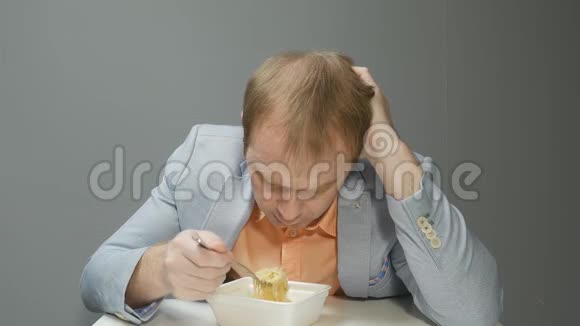 没有欲望的人吃方便面一个穿着蓝色夹克和金发的年轻人正悲伤地慢慢地吃着面条视频的预览图