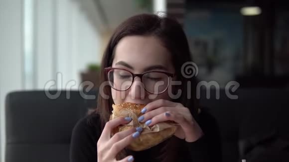 一个年轻的女人正在吃汉堡一个女孩坐在全景窗旁的咖啡馆里吃快餐视频的预览图