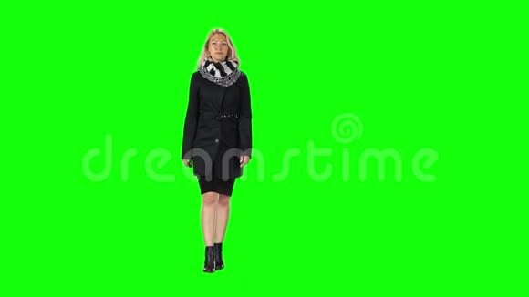 穿着黑色连衣裙外套围巾和靴子的金发女孩靠在绿色的屏幕上视频的预览图