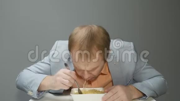 这个人很饿他很快就用叉子吃方便面穿蓝色夹克和橙色衬衫的人看上去视频的预览图