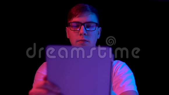 有平板电脑的年轻人一个男人在用平板电脑蓝色和红色的光落在黑色背景上的人身上视频的预览图