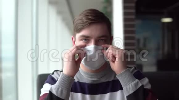 一个年轻人脱下医疗面具吃了一个汉堡然后戴上面具一个男人坐在窗边的咖啡馆里视频的预览图