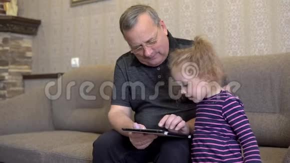 孙女和祖父坐着一块石碑女孩对平板皱着眉头一起坐在沙发上视频的预览图