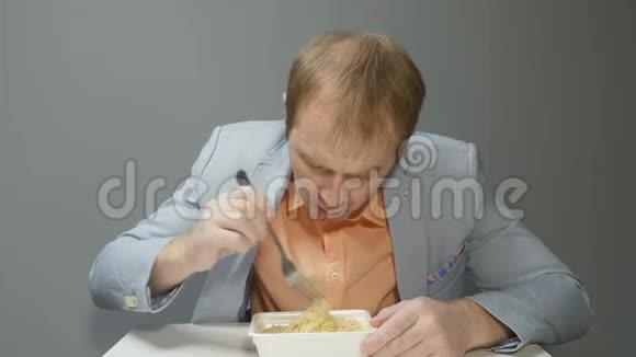 一个穿着蓝色夹克和橙色衬衫的年轻人正在吃美味的方便面他很饿我看着视频的预览图