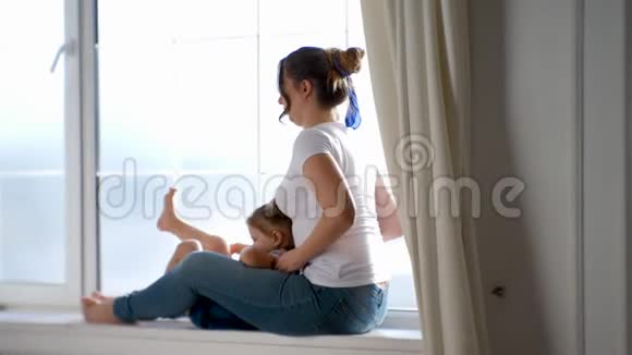 母亲和女儿穿着白色T恤衫坐在工作室的窗户上视频的预览图