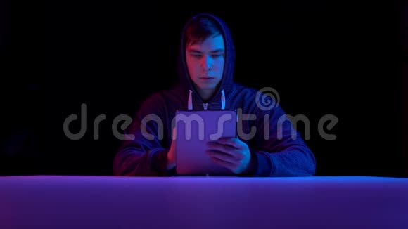 戴着平板电脑的年轻人黑客通过平板电脑进行黑客攻击蓝色和红色的光落在一个黑色的人身上视频的预览图