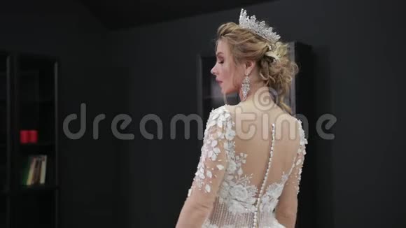 年轻的金发新娘穿着白色婚纱戴着皇冠在房间里摆着相机视频的预览图
