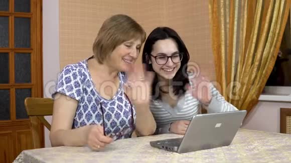 女儿和母亲通过笔记本电脑通过视频链接与朋友交流一个年轻的女人和一个老母亲视频的预览图