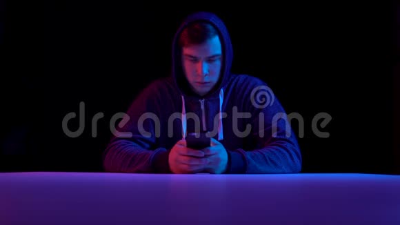 戴着智能手机的年轻人黑客通过电话攻击蓝色和红色的光落在一个男人身上视频的预览图
