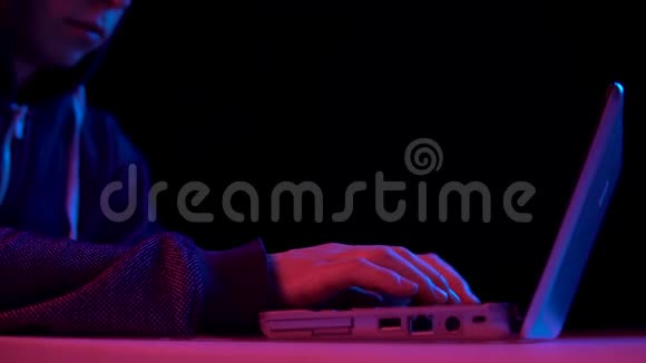 戴着笔记本电脑特写的青年黑客通过笔记本电脑进行黑客攻击蓝色和红色的光落在一个男人身上视频的预览图
