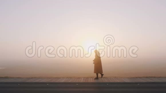 令人惊叹的宽背景拍摄的快乐旅游女人走在令人叹为观止的粉红色雾日落全景慢动作视频的预览图