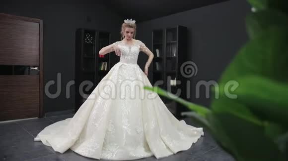 年轻的金发新娘穿着白色婚纱戴着皇冠在房间里摆着相机视频的预览图