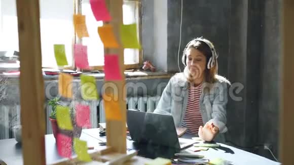 有创意的年轻女商人正在用耳机听音乐在办公桌前用笔记本电脑跳舞视频的预览图