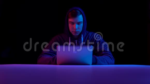 戴着笔记本电脑的青年黑客通过笔记本电脑进行黑客攻击蓝色和红色的光落在一个黑色的人身上视频的预览图