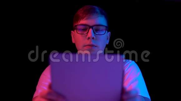有平板电脑的年轻人一个男人在用平板电脑蓝色和红色的光落在黑色背景上的人身上视频的预览图