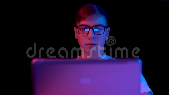 有笔记本电脑的年轻人男人用笔记本电脑蓝色和红色的光落在黑色背景上的人身上视频的预览图
