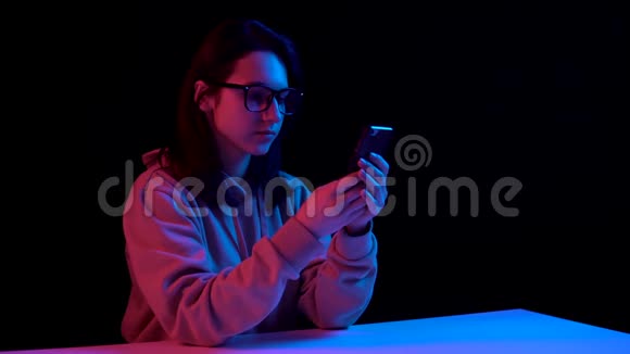 带着电话的年轻女人一个女人在打电话蓝色和红色的光落在黑色背景上的女人身上视频的预览图