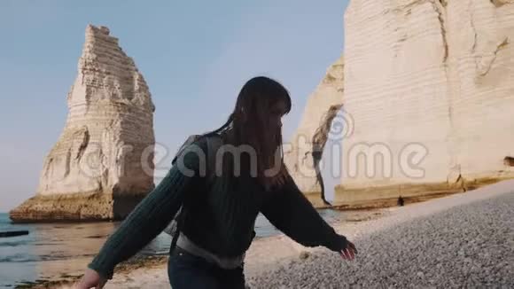 快乐微笑的黑发旅行者女人背包旋转手臂张开在岩石海岸附近的埃特雷塔缓慢运动视频的预览图