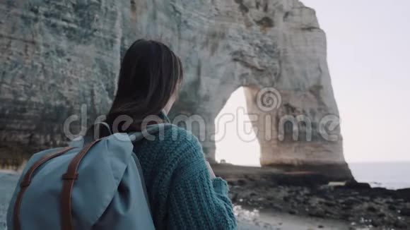 后景快乐的女游客带着背包在美丽平静的海边观看白拱岩在埃特雷特慢动作视频的预览图