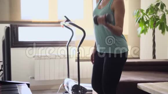 运动的年轻女子独自在客厅里用哑铃做运动穿运动装的女孩在家里训练身体健康视频的预览图