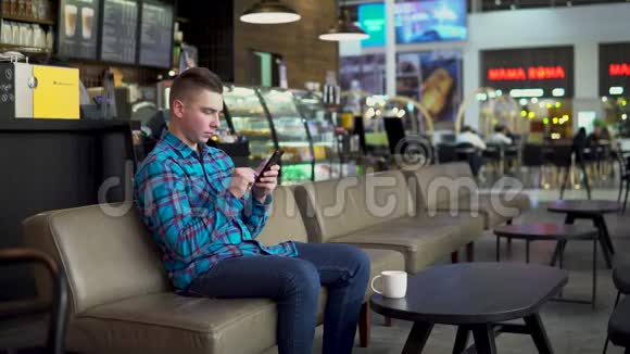一个年轻人正坐在一家带着电话的咖啡馆里这名男子在智能手机上通信喝咖啡特写镜头视频的预览图