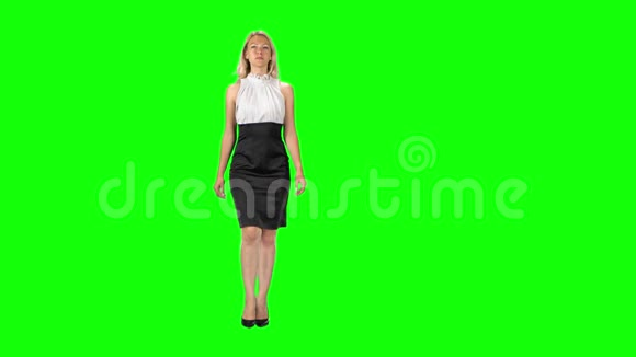穿着黑白色连衣裙和高跟鞋的金发女孩穿着绿色的屏幕视频的预览图
