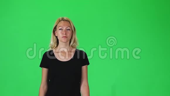 穿着黑色t恤的金发女孩在绿色屏幕上直视着相机慢动作视频的预览图