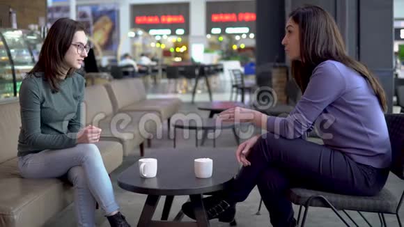 年轻的女人坐在咖啡馆里聊天妈妈和女儿坐在一起聊天喝咖啡视频的预览图