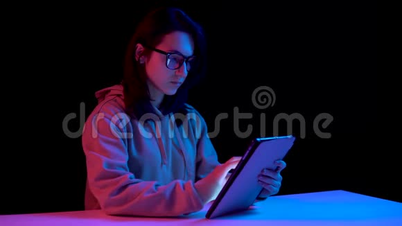 带着药片的年轻女人一个女人在用平板电脑蓝色和红色的光落在黑色背景上的女人身上视频的预览图