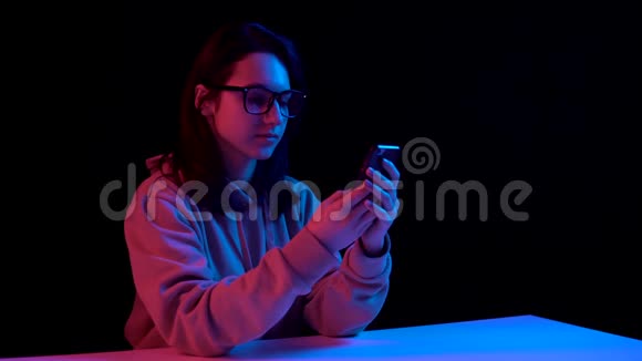 带着电话的年轻女人一个女人在打电话蓝色和红色的光落在黑色背景上的女人身上视频的预览图