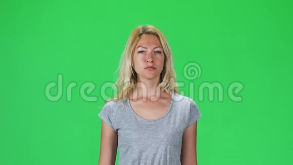 穿着灰色T恤的金发女孩在绿色屏幕上直视着相机慢动作视频的预览图
