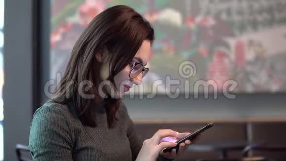 一个年轻的女人坐在一家带着电话的咖啡馆里女孩在智能手机上通信喝咖啡关闭视频的预览图