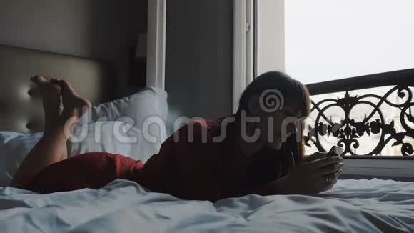 美丽的微笑黑发商务女性使用智能手机移动办公应用程序在床上与埃菲尔铁塔观景慢运动视频的预览图