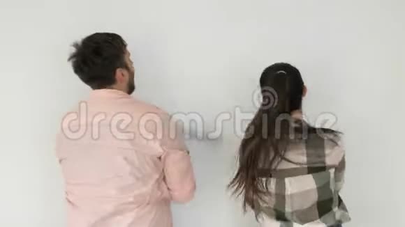 这对年轻夫妇画了一堵白色的墙男人和女孩站在一个房间的后面手里拿着滚轮视频的预览图