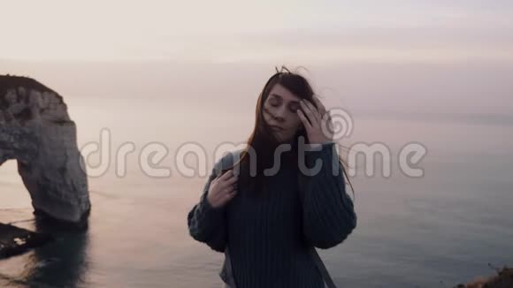 美丽平静的旅游女子看着相机转身看着绚丽的日落在埃特雷特悬崖上观看缓慢的运动视频的预览图