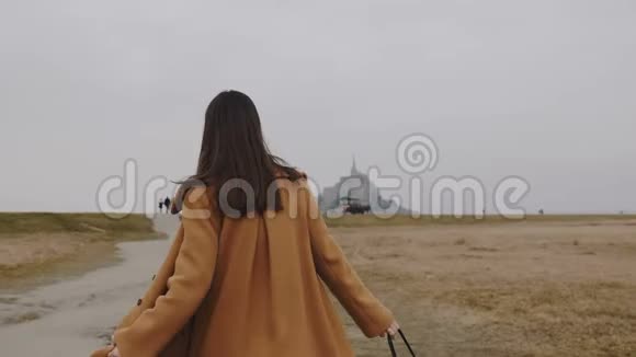 镜头跟随美丽优雅的女人步行到著名的蒙特圣米歇尔岛城堡阴天慢动作视频的预览图
