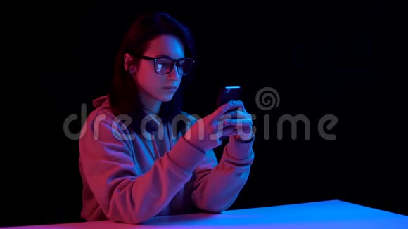 有智能手机的年轻女人女人用电话蓝色和红色的光落在黑色背景上的女人身上视频的预览图