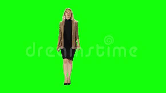 金发女孩穿着时尚的棕色夹克黑色连衣裙和高跟鞋穿着绿色的屏幕视频的预览图