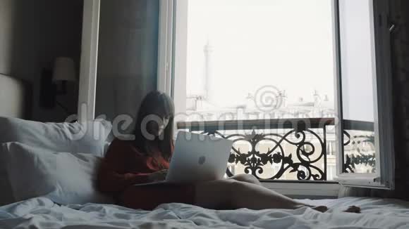 美丽成功的自由职业女性使用笔记本电脑在法国阳台床与埃菲尔铁塔观景慢运动视频的预览图