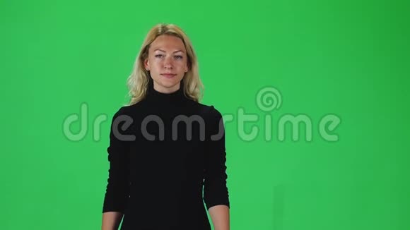 金发女孩穿着一件黑色连衣裙对着绿色的屏幕直视着相机慢动作视频的预览图