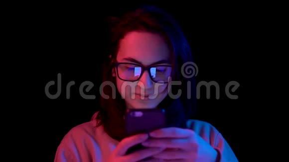 有智能手机的年轻女人女人用电话蓝色和红色的光落在黑色背景上的女人身上视频的预览图