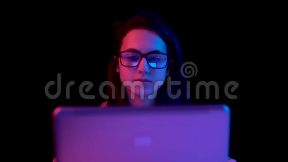 带着笔记本电脑的年轻女人一个女人在用笔记本电脑蓝色和红色的光落在黑色背景上的女人身上视频的预览图