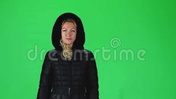 金发女孩穿着一件黑色的冬衣头罩靠在绿色的屏幕上慢动作视频的预览图