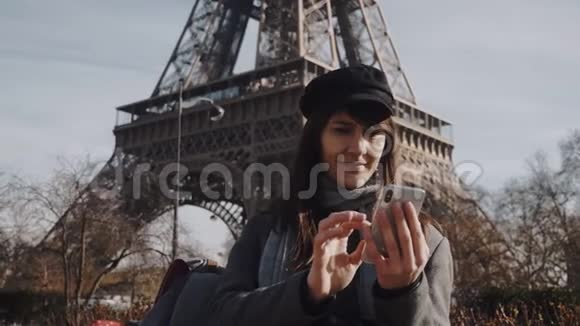 美丽的微笑年轻的欧洲妇女使用智能手机购物应用程序附近阳光明媚的秋天巴黎埃菲尔铁塔慢动作视频的预览图